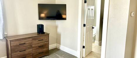 Una habitación con un aparador de madera, un televisor de pantalla plana montado en la pared y una puerta que da a otra estancia.