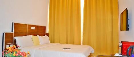 Une chambre d’hôtel avec un lit, une table de chevet, un miroir et une fenêtre avec des rideaux jaunes.