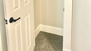 Une pièce avec une porte blanche, un placard avec une tringle et un sol recouvert d’une moquette.