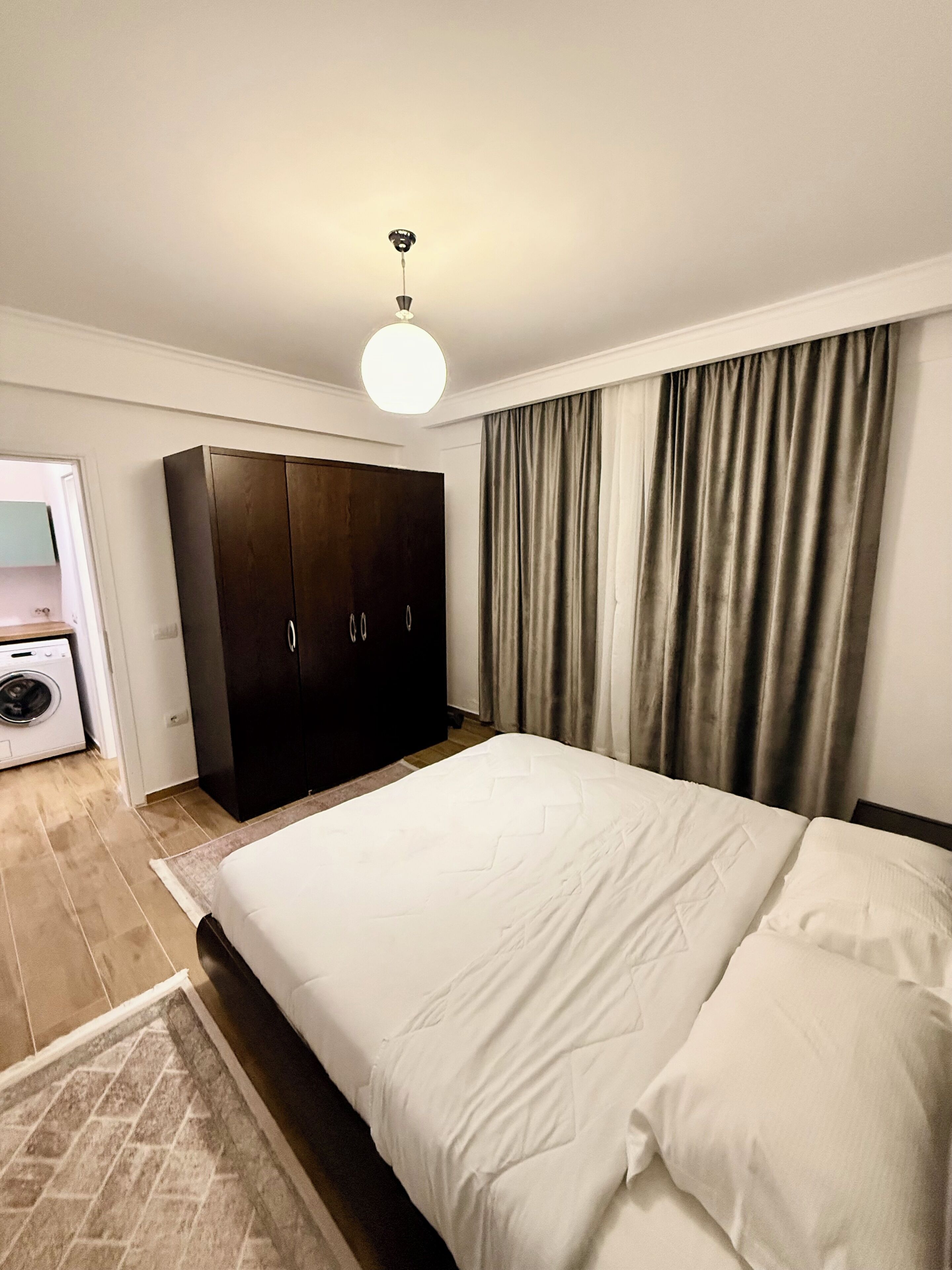 A bedroom with a bed, a wardrobe, a ceiling light, and a window with curtains.