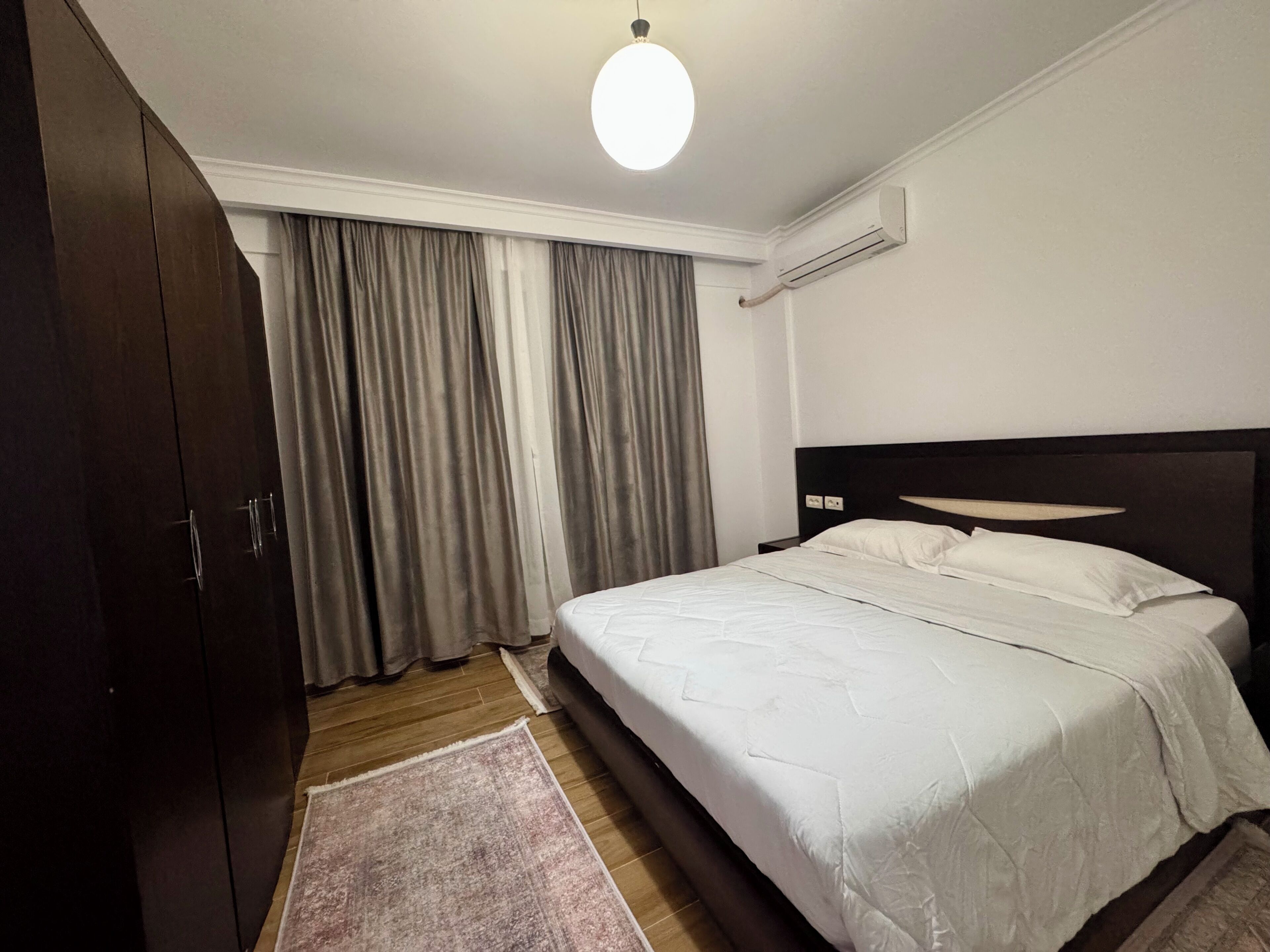Ein Schlafzimmer mit einem Bett, einem Kleiderschrank, einem Fenster mit Vorhängen, einer Klimaanlage und einer Lampe.
