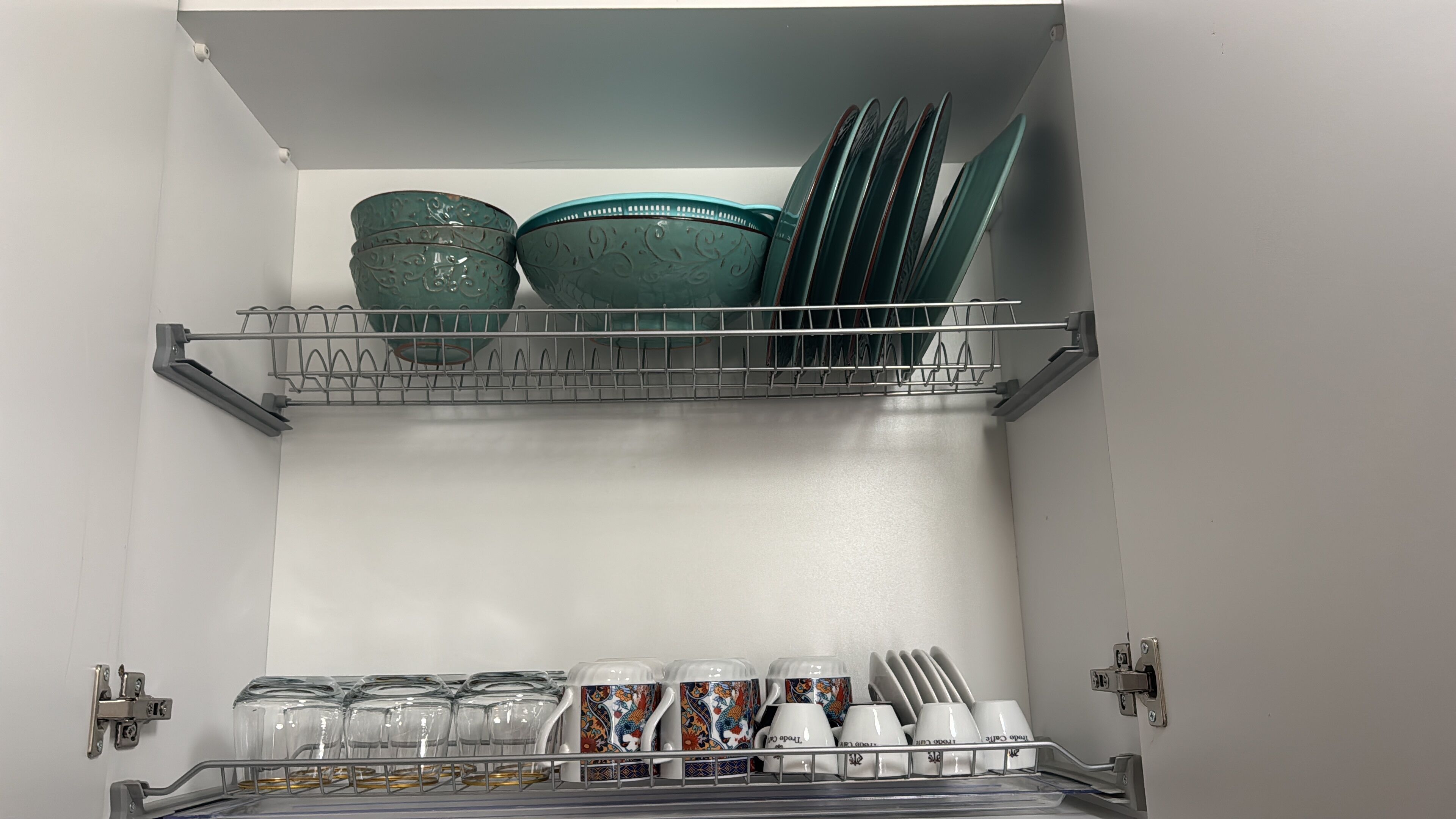 A kitchen with two shelves; the top shelf holds green bowls and plates, and the bottom shelf has glass jars and white mugs.