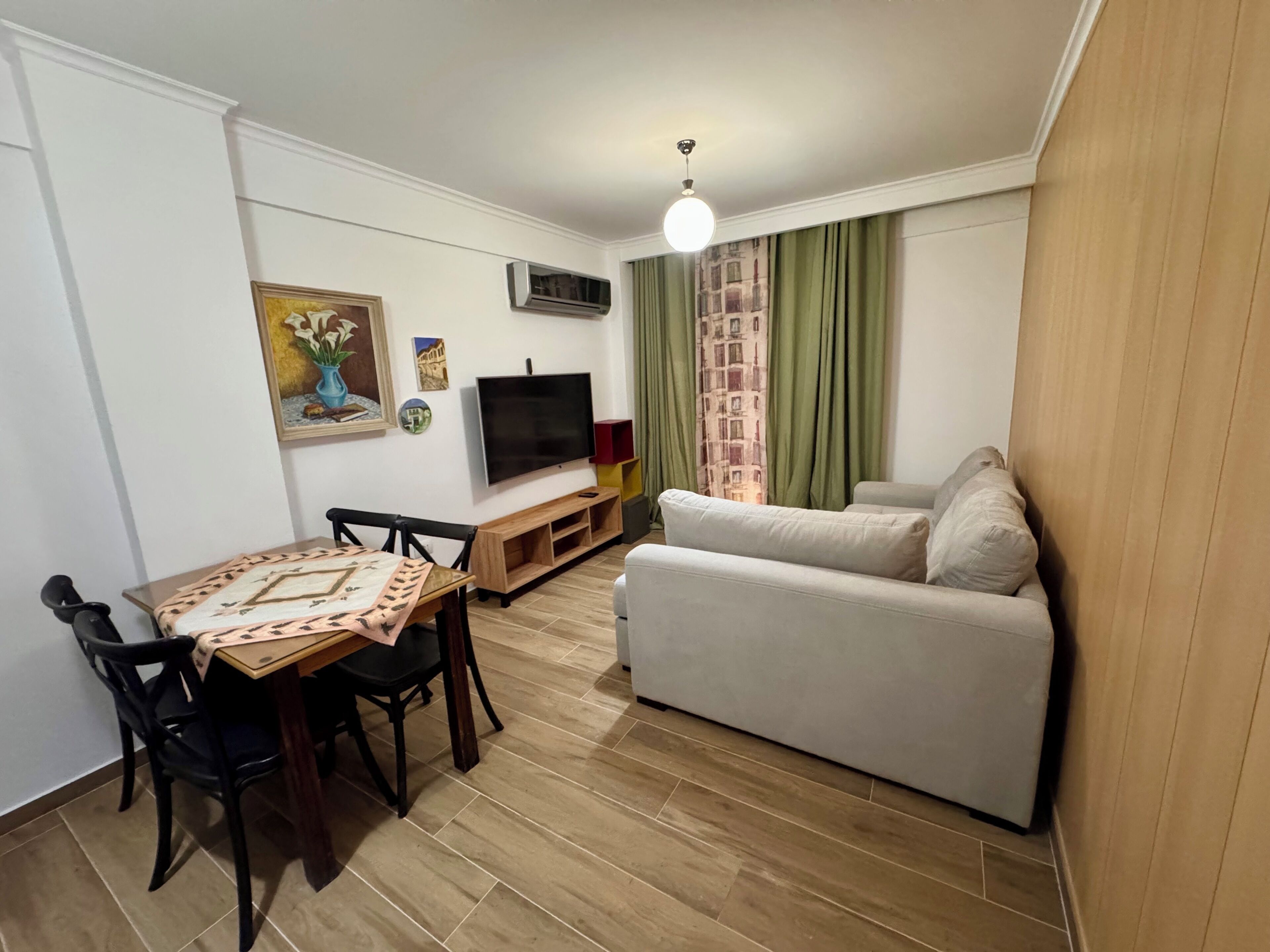 Una sala de estar con sofá, televisión, mesa de comedor, sillas y un cuadro en la pared.
