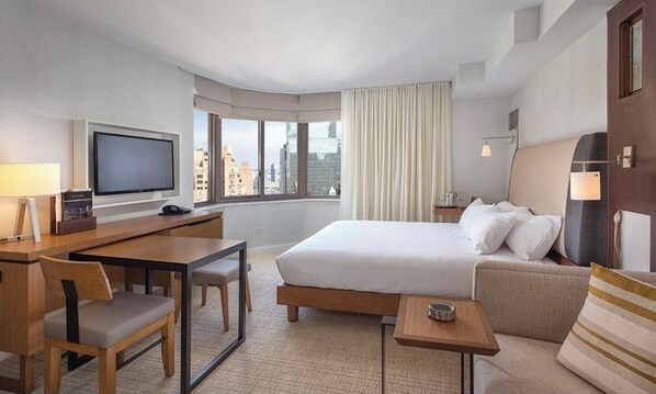 Ein Hotelzimmer mit Bett, Schreibtisch, Stuhl, Fernseher und Blick auf die Stadt.