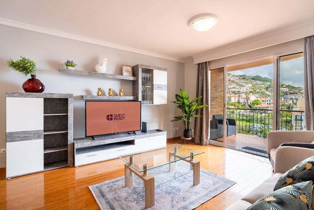 Een moderne woonkamer met een flatscreen televisie, een glazen salontafel, een bank en een balkon met uitzicht op de stad.