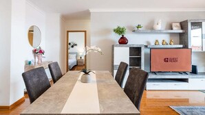 Un espace de restauration moderne avec une longue table, des chaises, un vase de fleurs, un miroir et une cheminée sur laquelle est posé un panneau indiquant « PRÊT POUR LES INVITÉS ».