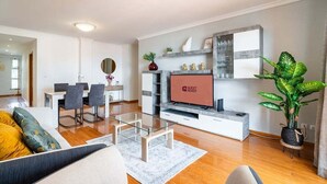 Un salon moderne comprenant un coin repas, un téléviseur à écran plat et une grande plante en pot.