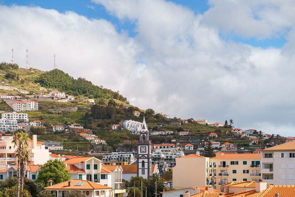 Una cittadina costiera con edifici, un'imponente torre dell'orologio e uno sfondo collinare.