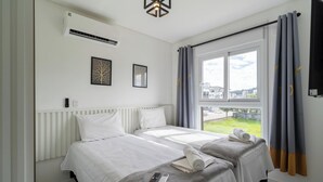 A hotel room with two beds, a radiator, an air conditioner, a window with curtains, and a view of buildings. - Apts in a Condominium w/ Pool Just 500 m fr Ingleses Beach - Mncs (Florianópolis)
