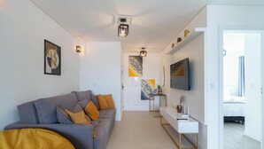 A modern living room with a grey sofa, a small white table, and a TV mounted on the wall. - Apts in a Condominium w/ Pool Just 500 m fr Ingleses Beach - Mncs (Florianópolis)