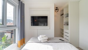 A bedroom with a bed, a TV mounted on the wall, a window with curtains, and a built-in wardrobe. - Apts in a Condominium w/ Pool Just 500 m fr Ingleses Beach - Mncs (Florianópolis)