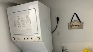 Eine Waschmaschine und ein Trockner mit Bedienungsknöpfen, einem Stromkabel und einem 'Wascherei'-Schild an der Wand.