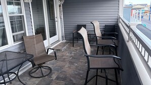 Eine überdachte Terrasse mit Gartenmöbeln, einer Glasschiebetür und Blick auf die Straße.