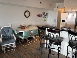 A dining area with a table and chairs, a clock on the wall, and a refrigerator in the background. - Spacious 3-bedroom condo on the boardwalk with fantastic views. (Wildwood)