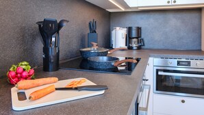 A modern kitchen with a stove, coffee maker, and a cutting board with carrots.