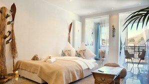 A bedroom with a bed, pillows, a bedside table, a wooden chest, and a view of the outdoors.
