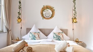 A hotel room with a bed, pillows, a bedside table, a wall-mounted mirror, and hanging lights.