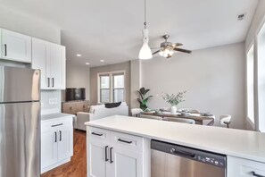 A modern kitchen with white cabinetry, a stainless steel refrigerator, a dishwasher, a dining area with a table and chairs, and a ceiling fan. - MTR~TopFloor~Patio~PetFriendly~FreeParking (Chicago)