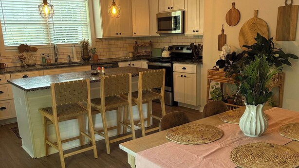 A kitchen with a central island, wooden chairs, a dining table with placemats, and hanging pendant lights. - Cute & Cozy 2 Bdrm Getaway  Close to Downtown (Greer)