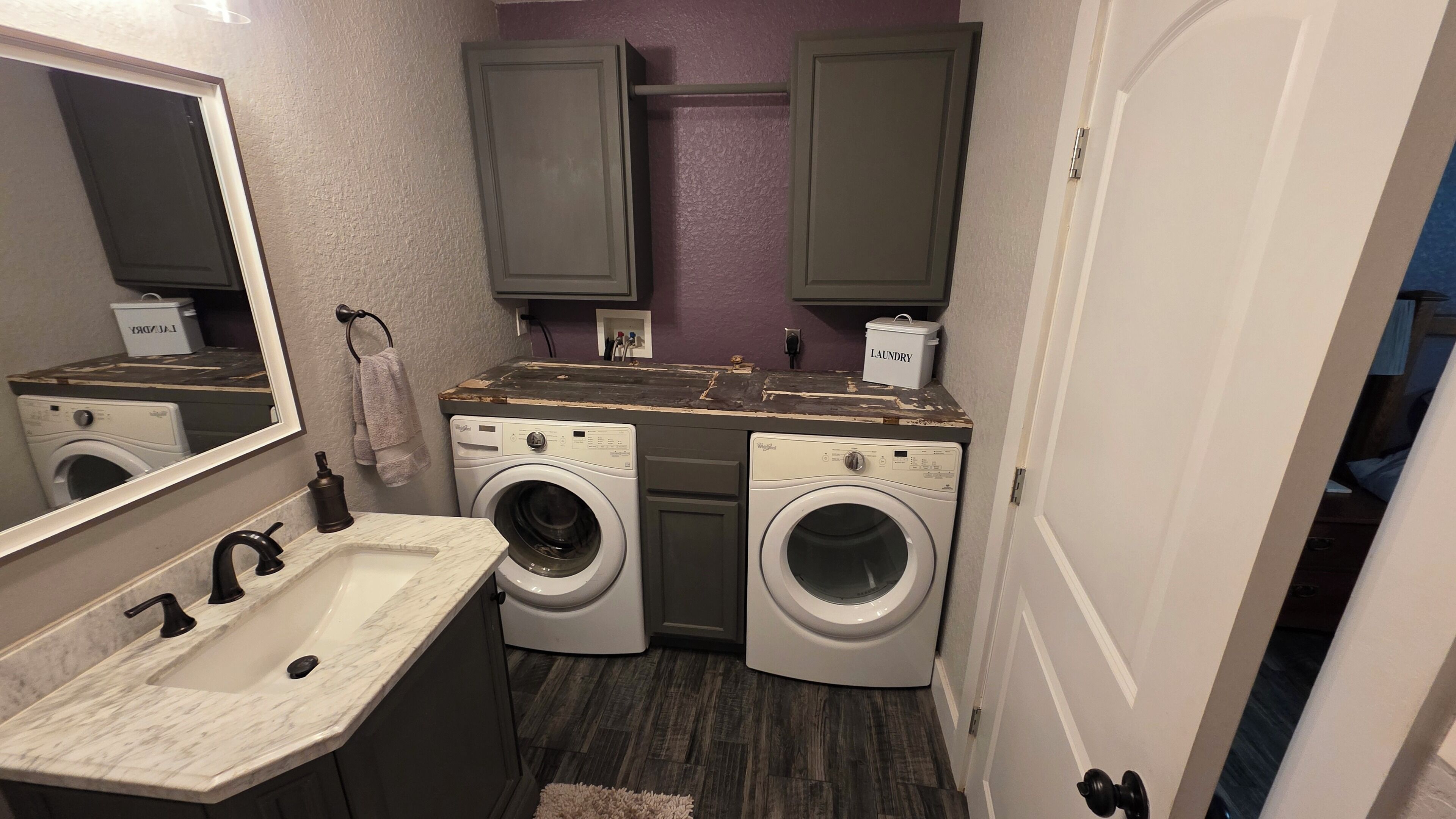 A compact laundry room with two washing machines, a sink, and a mirror.