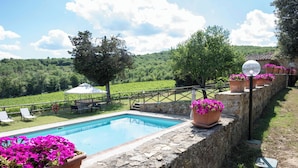 A swimming pool with a stone wall, potted flowers, and a view of a vineyard. - Villa nestled in the vineyards of chianti with private pool (Pieve A Presciano)