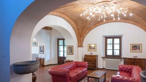 A spacious living room with a red leather sofa, a coffee table, and a stone basin. - Villa nestled in the vineyards of chianti with private pool (Pieve A Presciano)