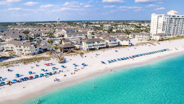 Eine Küstenregion mit Strandhäusern, einem Sandstrand und klarem, türkisblauem Wasser.