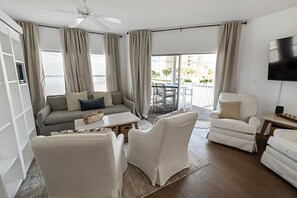 A modern living room with a sofa, two armchairs, a coffee table, and a TV mounted on the wall. - Beachwalk Bliss at Sandpiper Cove Unit 9216 – Gulf Views & Steps to the Beach! (Destin)