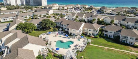 A resort with a central swimming pool, multiple buildings, and a view of the ocean.