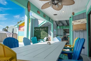 A beach-themed restaurant with outdoor seating, a ceiling fan, and a sign reading 'Listen to the palms.' - Casa Linda: Pool, Arcade & Sun Decks (Jensen Beach)