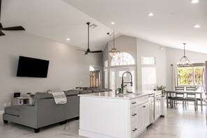 A modern kitchen with white cabinetry, a central island, and a dining area with a table and chairs. - Pool, Park, & Ramp! Book today! (Port St. Lucie)