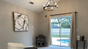 A living room with two chairs, a small table, a chandelier, a bar area, and a view of a swimming pool. - Pool, Park, & Ramp! Book today! (Port St. Lucie)