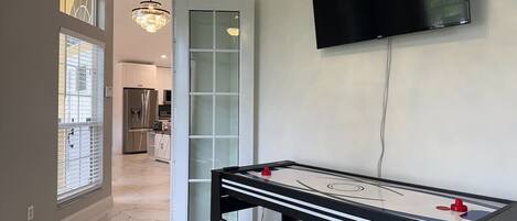 Une pièce équipée d’un baby-foot, d’un téléviseur fixé au mur et d’une porte donnant sur une autre pièce.