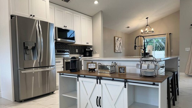 A modern kitchen with stainless steel appliances, a wooden island, and a view of the outdoors. - Pool, Park, & Ramp! Book today! (Port St. Lucie)