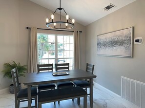 A dining area with a table, chairs, a chandelier, a window with curtains, and a radiator. - Pool, Park, & Ramp! Book today! (Port St. Lucie)
