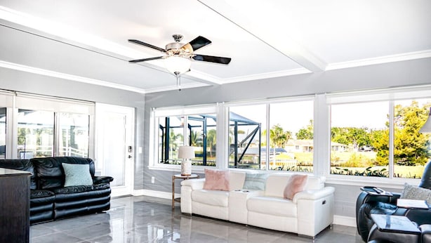 Uma sala de estar ampla com ventilador de teto, dois sofás, uma mesa de centro e grandes janelas com vista para o exterior.