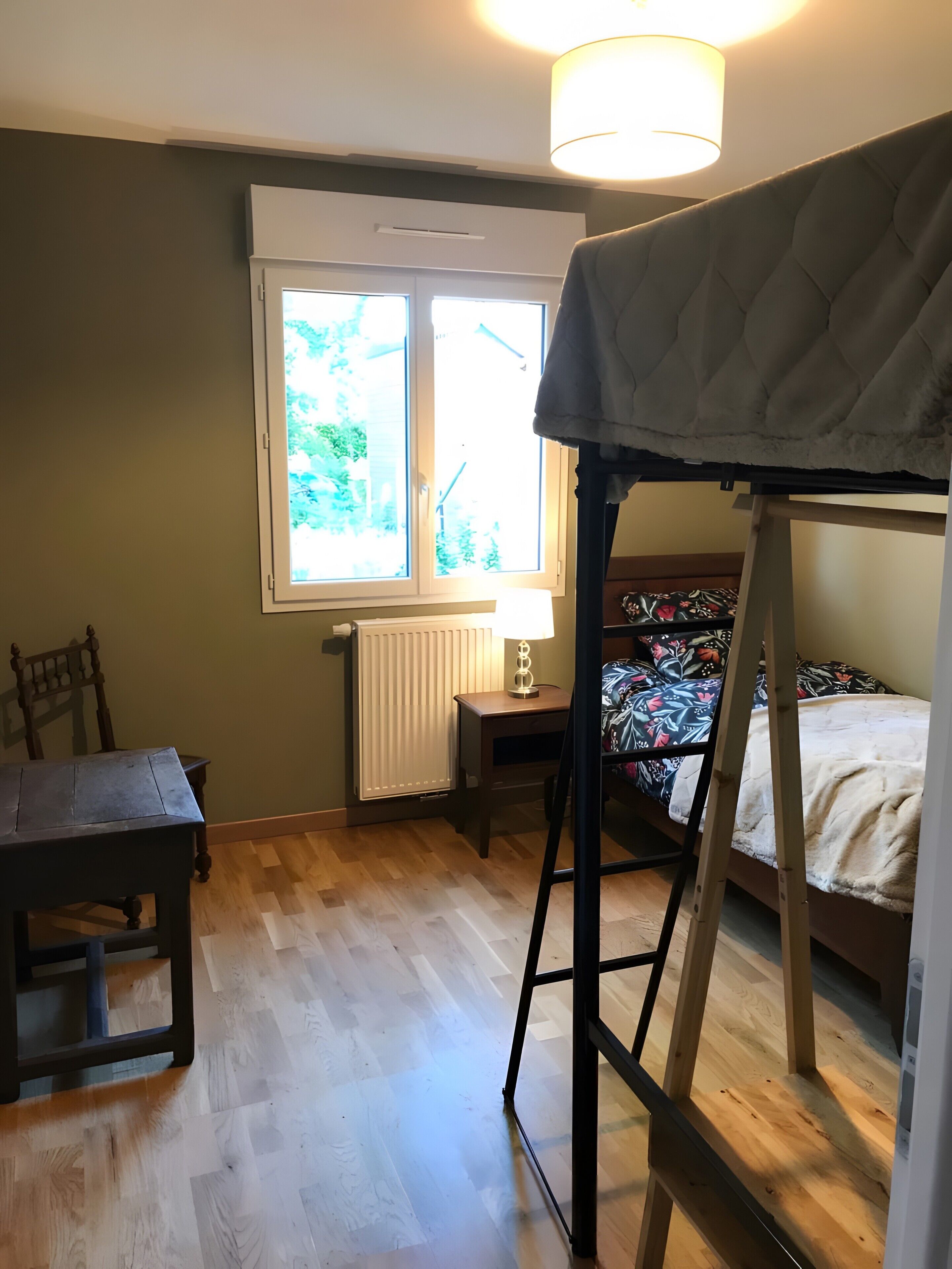 A room with a bunk bed, a desk with a lamp, a chair, and a radiator.