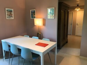 A dining area with a white table, blue chairs, a red folder, and a floor lamp. - Holiday Home 'Logis Des 2 Chênes' with Private Terrace, Private Garden and Wi-Fi (Forges-les-Eaux)