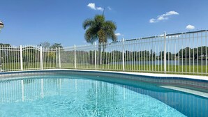 En klar blå swimmingpool omgivet af et hvidt hegn, med en palme og en blå himmel i baggrunden.