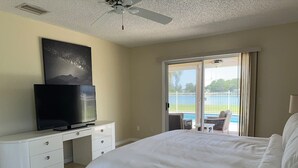 Et hotelværelse med en seng, et fjernsyn på en hvid kommode, en loftsvifte og en balkon med havudsigt.