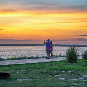 A couple taking a photo at sunset by a lakeside walkway. - Chincoteague Bay RV Resort & Cottages (Chincoteague)
