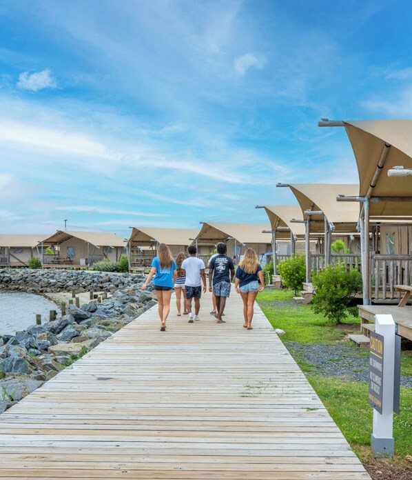A wooden boardwalk leading to beachside accommodations with overwater bungalows and a rocky shoreline. - Chincoteague Bay RV Resort & Cottages (Chincoteague)