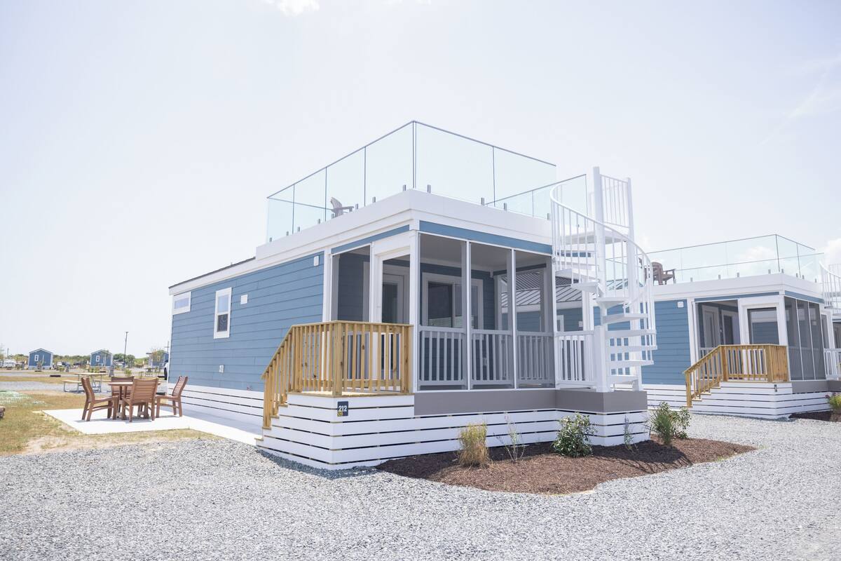 A modern, two-story house with a balcony, a porch, and a small outdoor seating area.