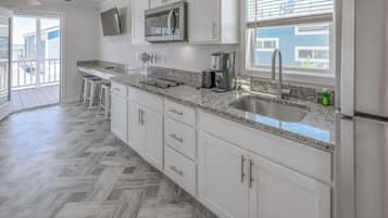 A modern kitchen with white cabinets, a granite countertop, a stainless steel sink, and a built-in microwave.