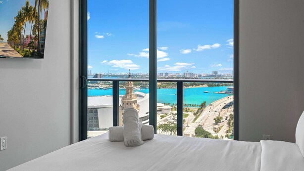 A hotel room with a large window, a bed, and a painting on the wall. - Sleek 1BR | Bay Views | Walk to Kaseya Center (Miami)