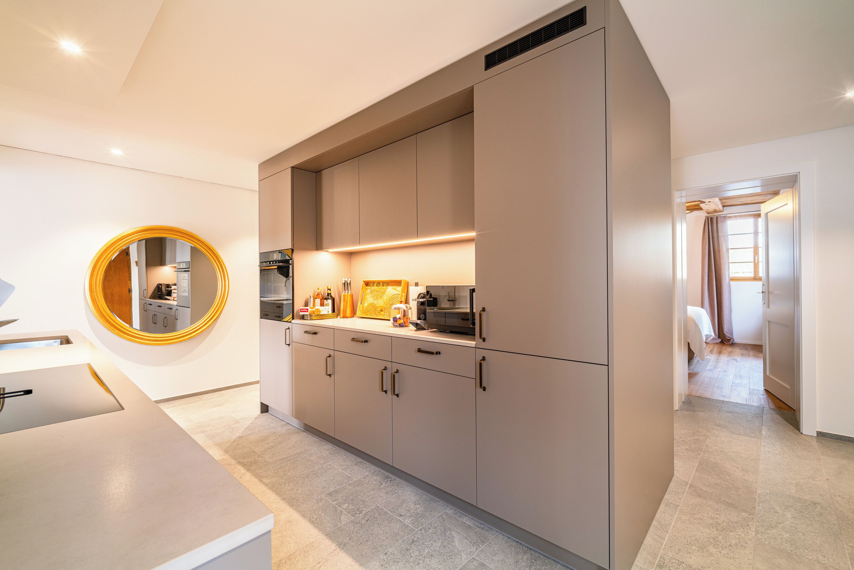 A modern kitchen with built-in cabinets, a countertop, and a round mirror.