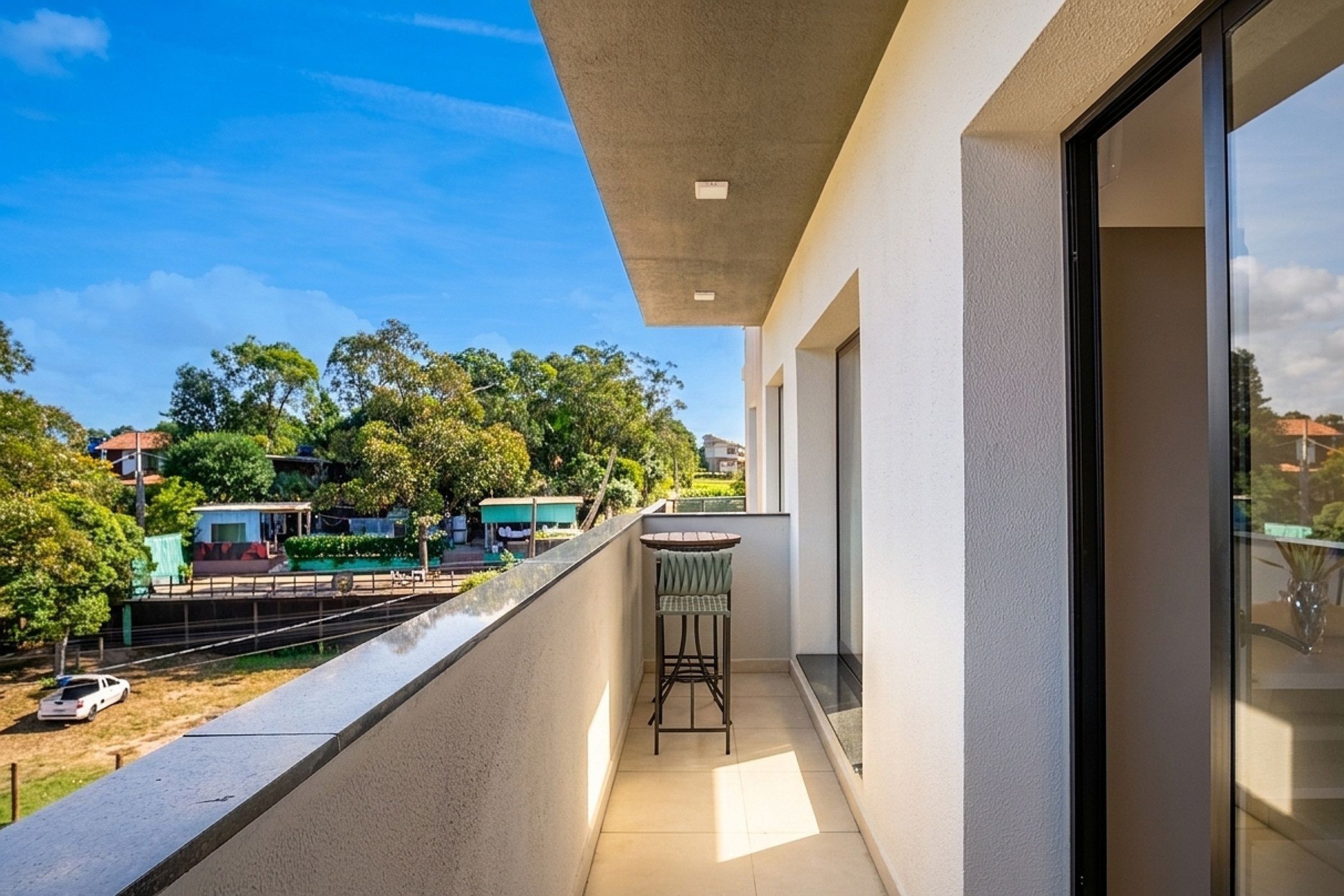 A balcony with a view of a residential area, a small table, and a chair.