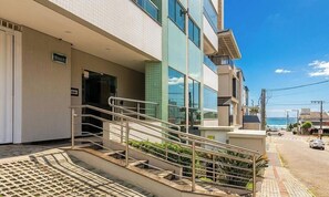 A modern building with a staircase leading to a balcony, a clear view of the ocean, and a street with cars. - Apt. w/ AC in Trindade, Floripa Tst001 (Florianópolis)