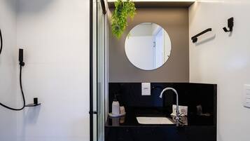Un baño moderno con una encimera negra, un espejo redondo y un cabezal de ducha de mano.