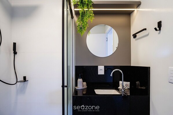 Un baño moderno con encimera negra, espejo redondo, grifo y planta colgante.